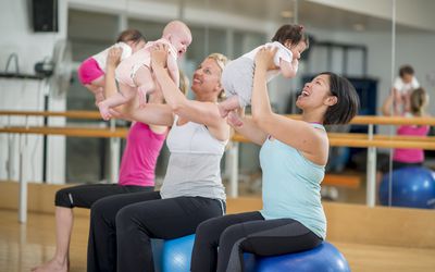 在健身课上，把婴儿抱在健身球上的妇女。