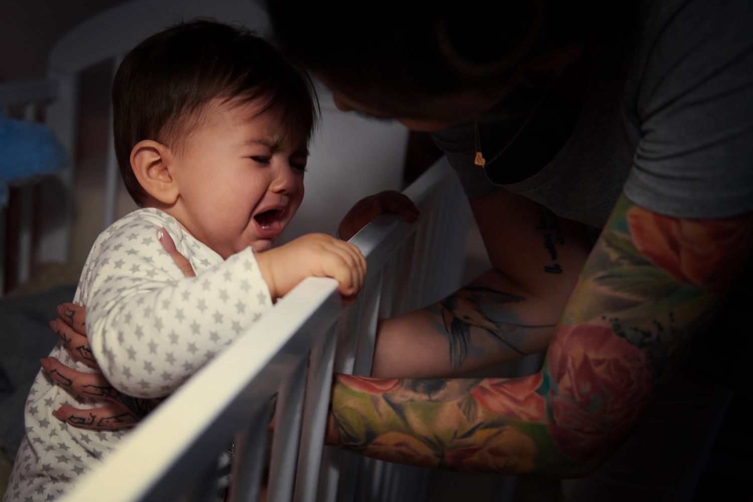 Parent tries to comfort crying baby in crib