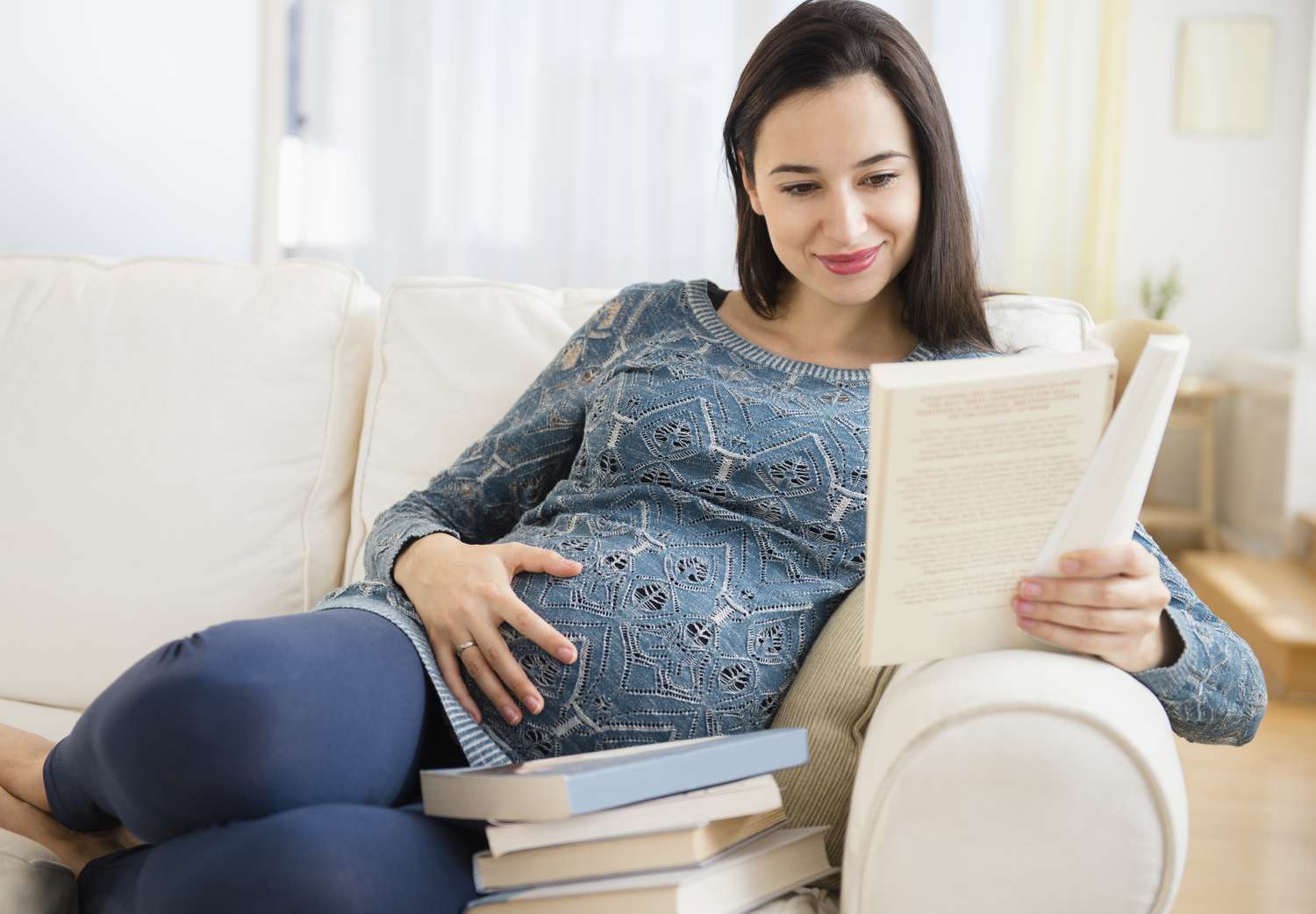 怀孕的白人妇女在沙发上读婴儿书