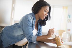 Pregnant woman eating peanut butter in kitchen