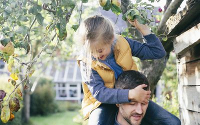 女儿骑在父亲的肩上，从树上摘苹果