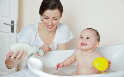 Mum pouring soap on hand, baby in bathtub