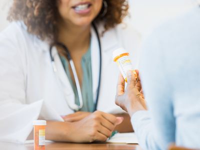 Close up of a patient holding pill bottle talking to a doctor