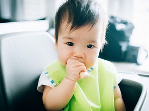 可爱的婴儿吃婴儿手指饼干在高椅子上存货照片