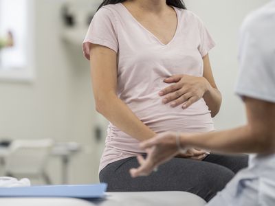 image of a pregnant person holding belly and sitting on a doctor's table