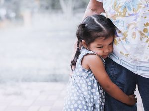 Sad little girl hugging her mother's leg