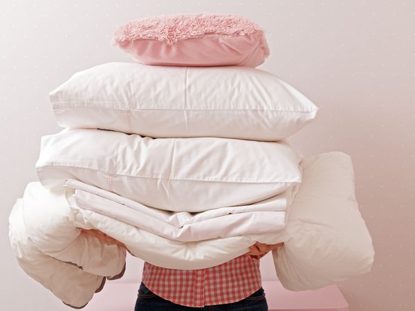 Woman holding a pile of bedding for sleeping. Household