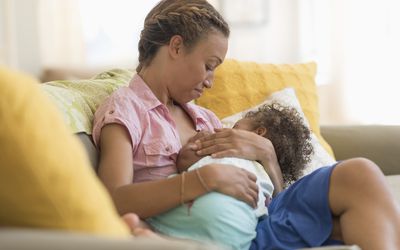 Black woman nursing daughter in living room