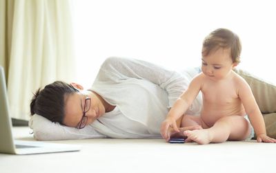 妈妈和宝宝躺在地板上拿着笔记本电脑和手机
