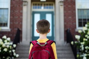 小男孩背着双肩包站在教学楼前