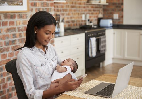 一名妇女抱着新生儿，手提电脑和手机