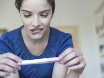 Woman holding home pregnancy test and looking worried