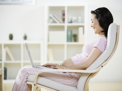 Pregnant woman using laptop, smiling, side view