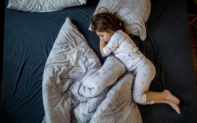 一个小女孩斜着毛毯和枕头睡在床上