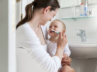 Mother brushing baby's teeth in bathroom