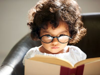 Little girl wearing glasses and reading a book