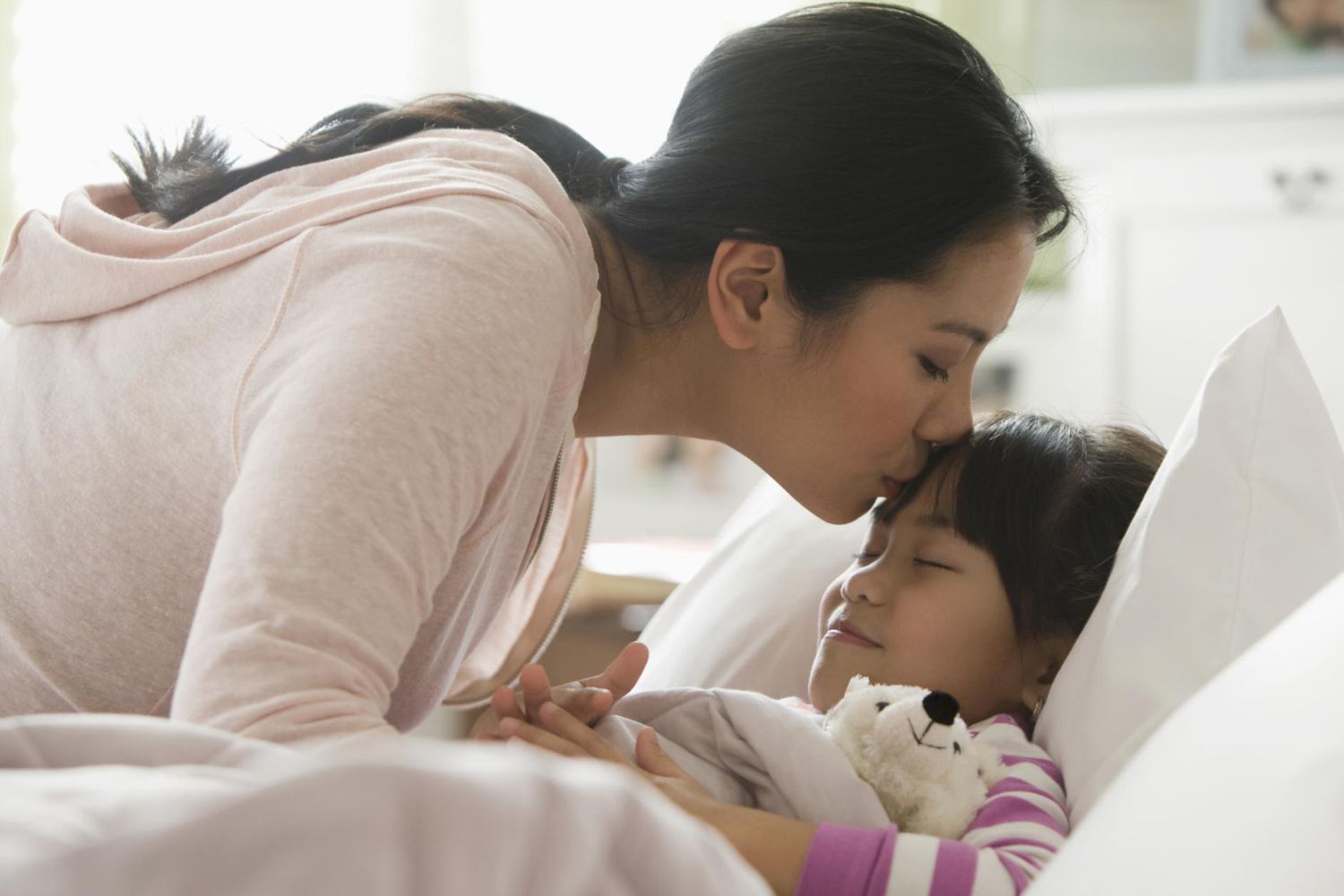 一个sian mother comforting daughter in bed.