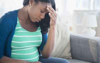 焦虑的黑人孕妇在沙发上摩擦额头