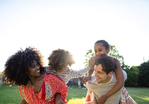 A woman and a man each carry a child on their back while smiling.