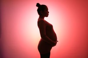 A pregnant person is seen in silhouette, holding their belly.