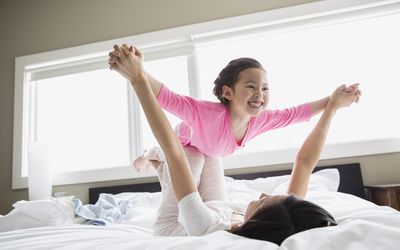 Girl playing airplane with mom on a bed