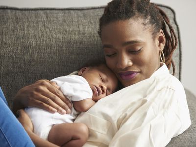 Black mother cuddling sleeping baby son on sofa