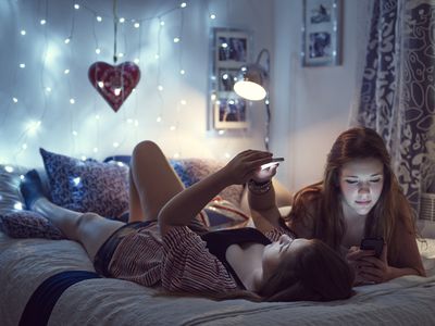 Two teens on a bed looking at their phones