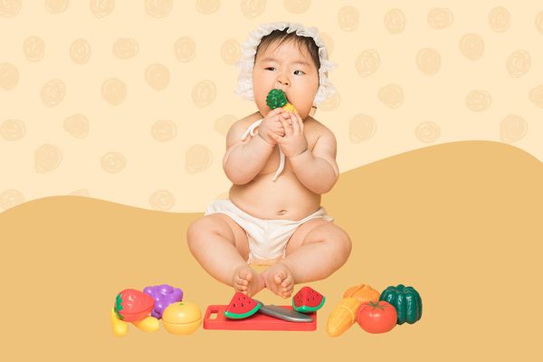 6-Month Old baby playing with a cutting fruit set on an orange background