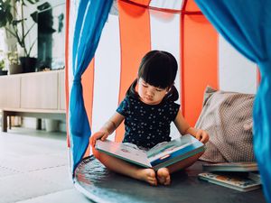 女孩在家里享受自己的闲暇时光。她和她的泰迪熊在家里的帐篷里看书