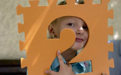 Little girl holding the foamed plastic frame of a number in front of her face