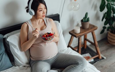 孕妇坐在床上吃浆果听音乐