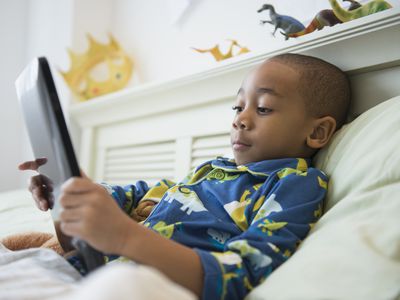 Young boy using digital tablet in bed