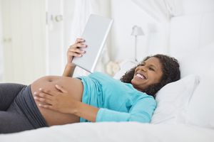 Pregnant woman using tablet computer on bed