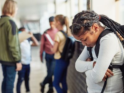 Young girl looking sad while being excluded from her peers in the hallway of a school