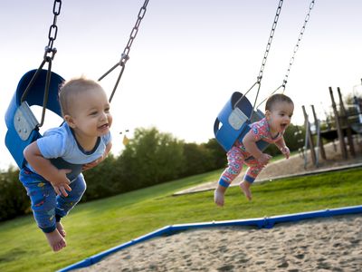 12 month old fraternal twins swinging in swings at a park