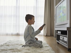 child holding remote sitting on rug in front of television