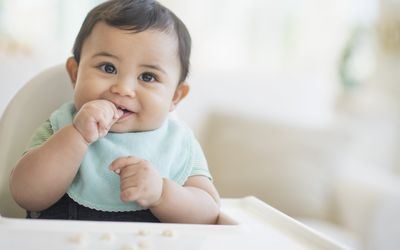 baby in high chair eating puffs