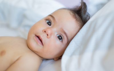 Baby boy laying on white bed looking at camera