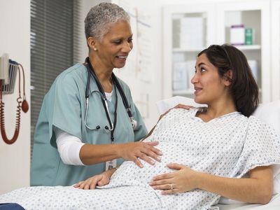 A pregnant woman in a hospital gown talking to her doctor in the hospital