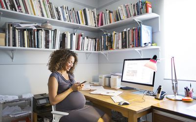 一个混合种族的孕妇工作在家坐在她的办公桌上使用电脑。