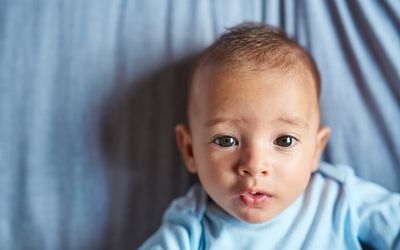 Baby wearing blue onesie on a blue sheet staring at the camera