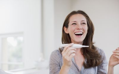 微笑的妇女拿着怀孕测试呈阳性华体会体育官方人口
