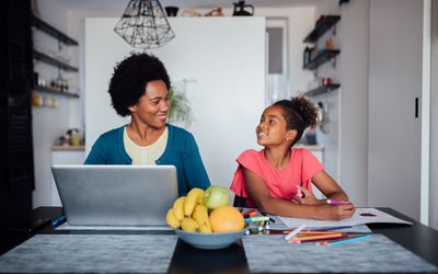 一个幸福的非裔美国家庭，成熟的母亲在家用笔记本电脑工作，而她的女儿在家上学做作业