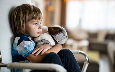 Sad boy embracing his teddy bear in home isolation.