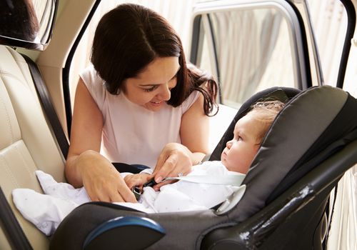 A mother buckling her baby into a carseat