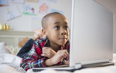 boy using laptop on a bed