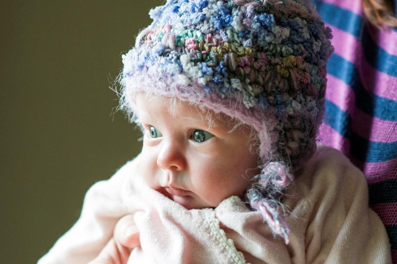 A newborn infant girl (age 3 weeks) wearing a homemade knitted hat, while being held by her mother.