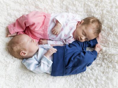 Newborn twins sleeping on white blanket