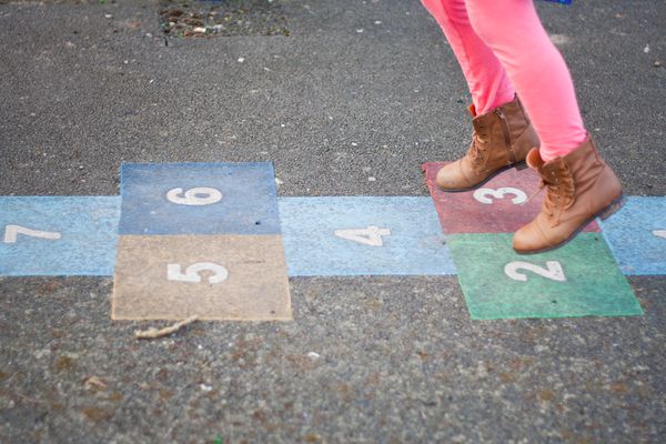 Person playing hopscotch on pavement while wearing brown boots and pink leggings