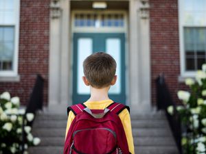 一个小男孩背着书包站在学校大楼前